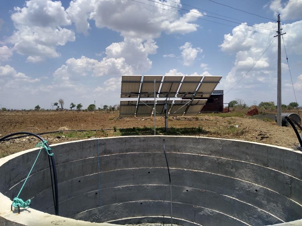 Solar panels powering an agricultural water pump beside a well